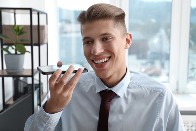 Photo of Young man with smartphone listening to voice message in office