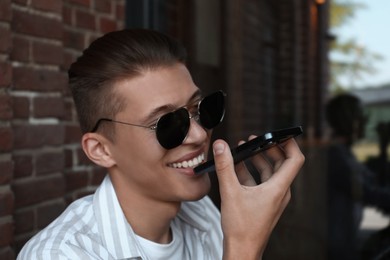 Young man recording voice message via smartphone in outdoor cafe