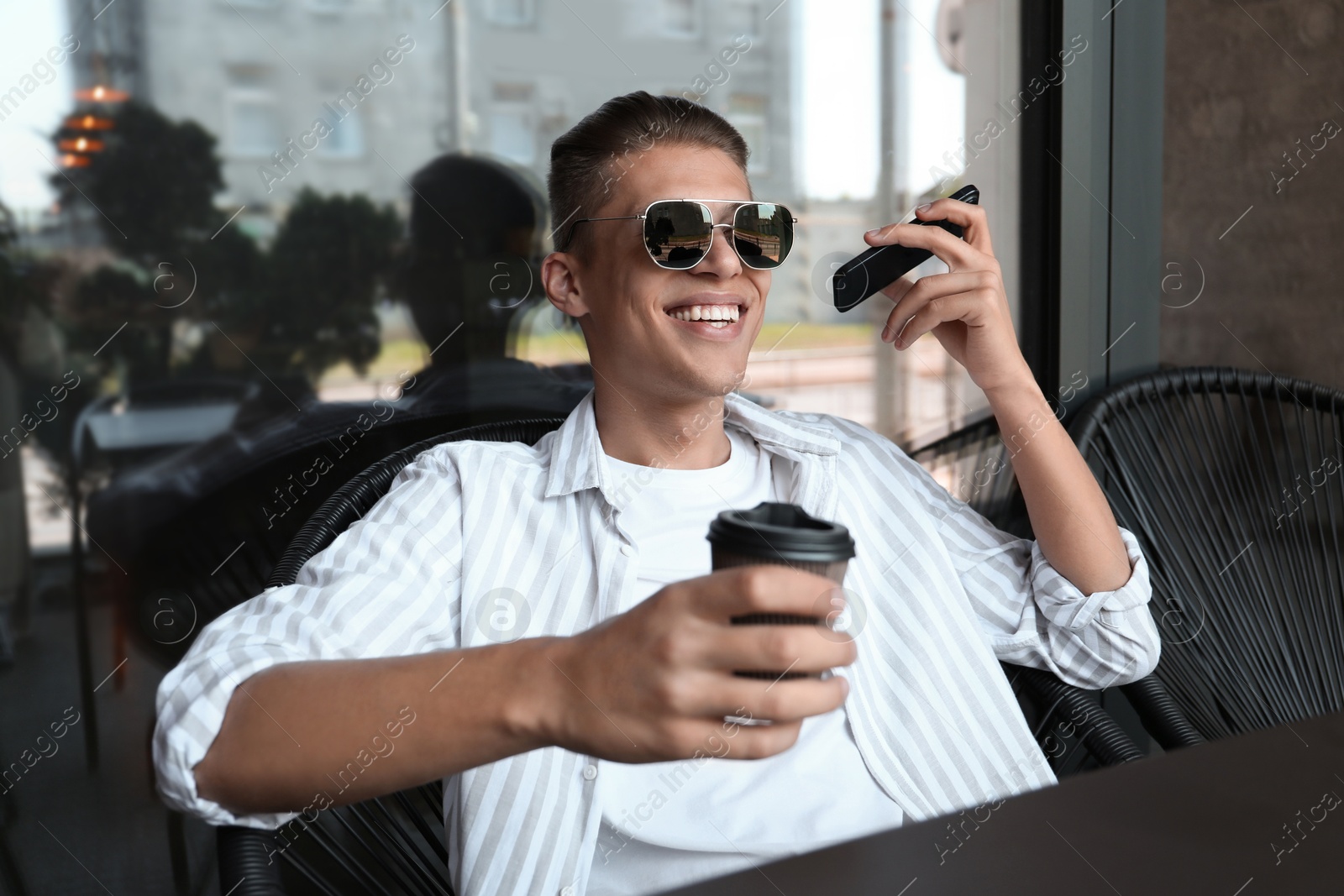 Photo of Young man with smartphone listening to voice message in outdoor cafe