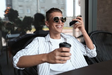 Young man with smartphone listening to voice message in outdoor cafe