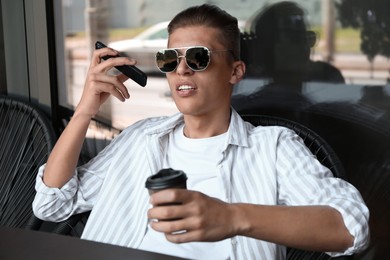 Young man with smartphone listening to voice message in outdoor cafe