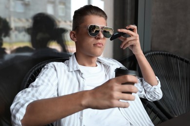 Young man with smartphone listening to voice message in outdoor cafe