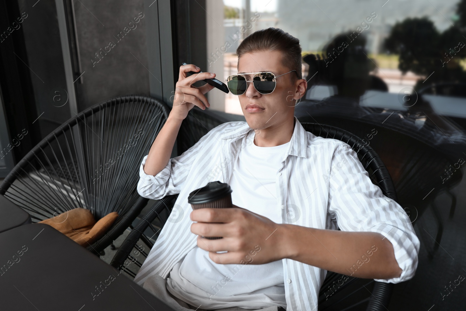 Photo of Young man with smartphone listening to voice message in outdoor cafe