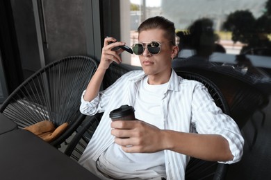 Photo of Young man with smartphone listening to voice message in outdoor cafe