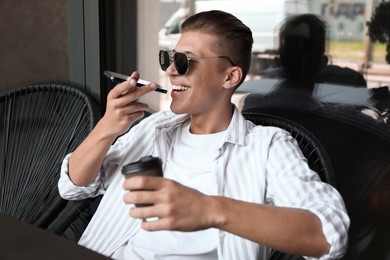 Photo of Young man recording voice message via smartphone in outdoor cafe