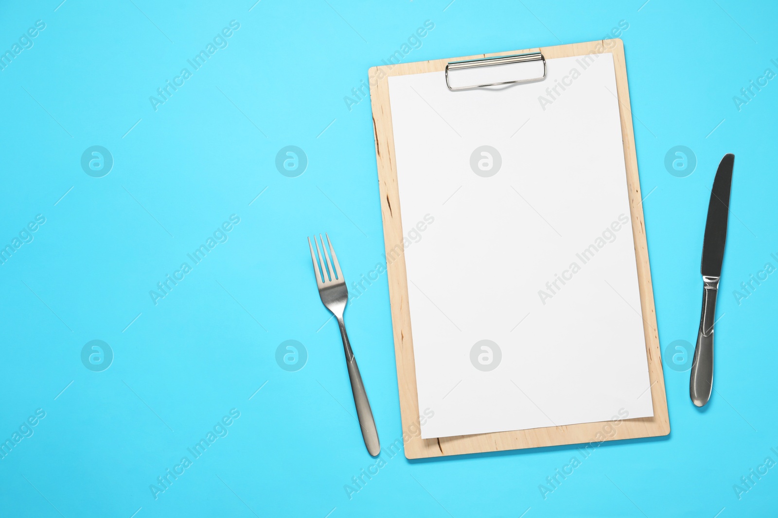 Photo of Clipboard with empty paper for menu design and cutlery on light blue table, flat lay. Space for text