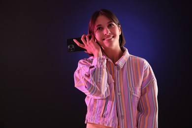 Photo of Beautiful woman listening to voice message via smartphone on dark background with neon lights, space for text