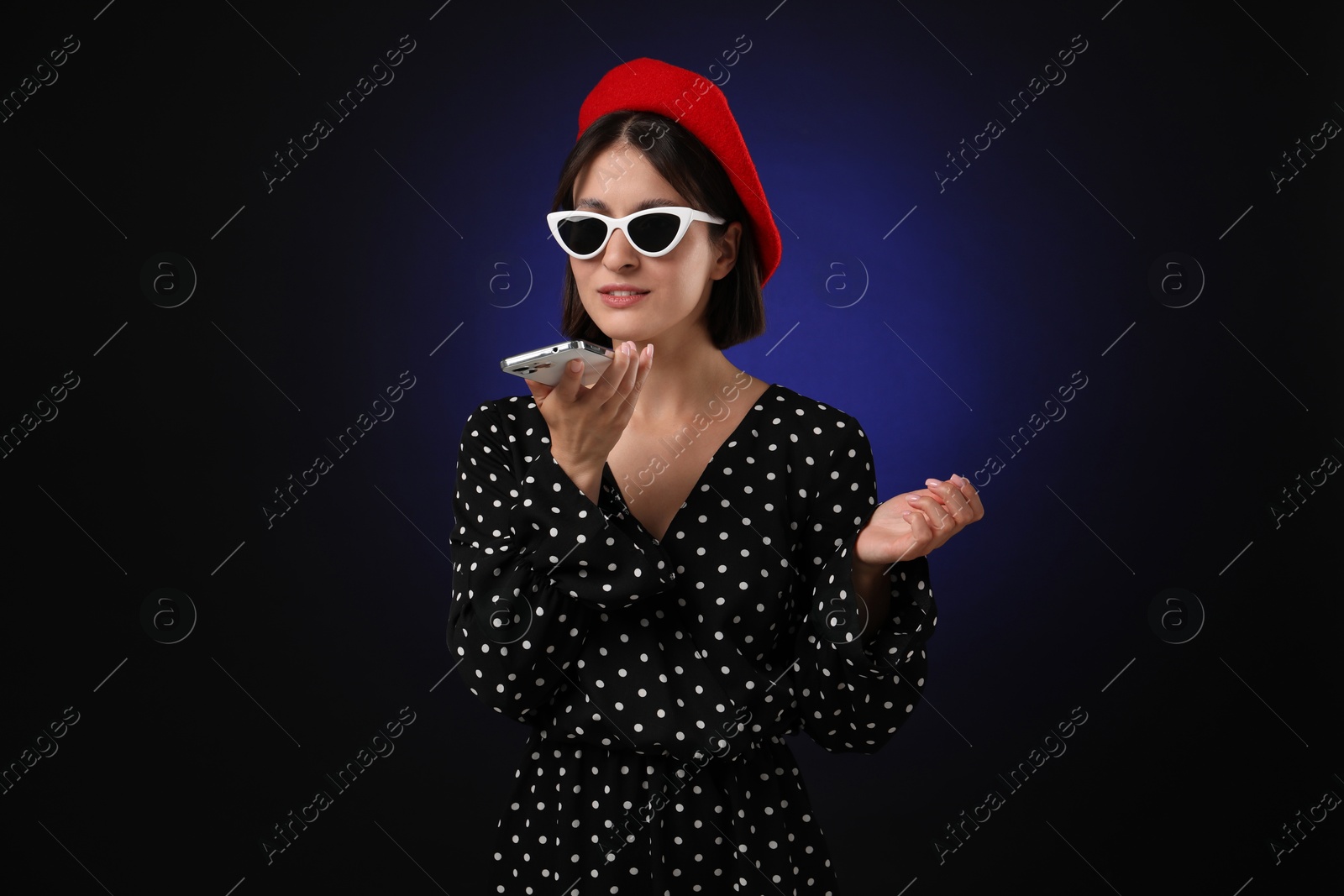 Photo of Stylish woman recording voice message via smartphone on dark background