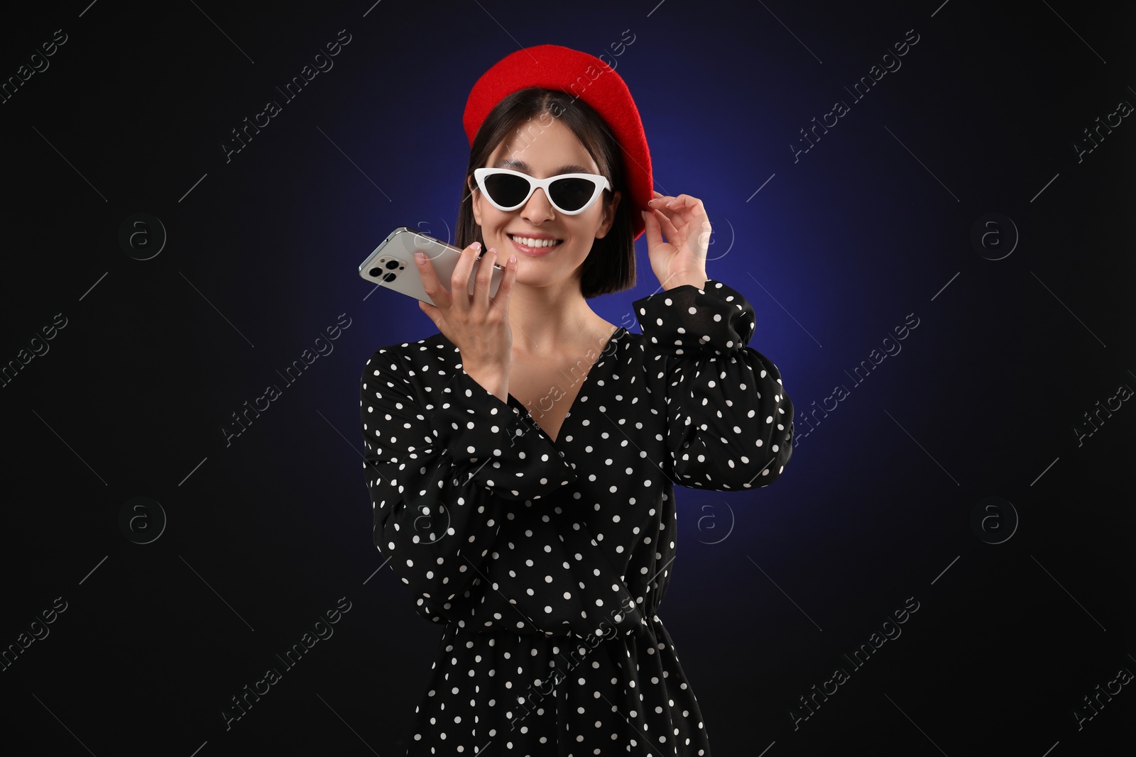 Photo of Stylish woman recording voice message via smartphone on dark background