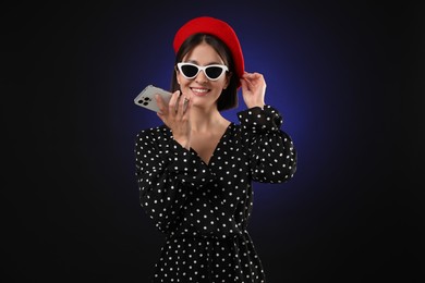 Stylish woman recording voice message via smartphone on dark background