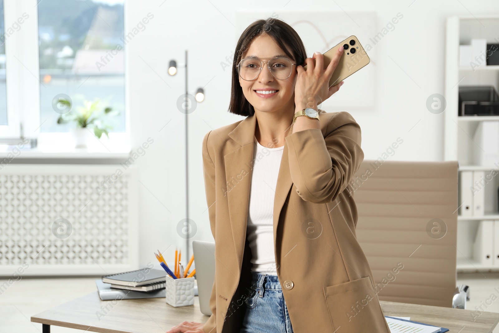 Photo of Beautiful woman with smartphone listening to voice message in office