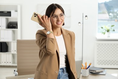 Photo of Beautiful woman with smartphone listening to voice message in office