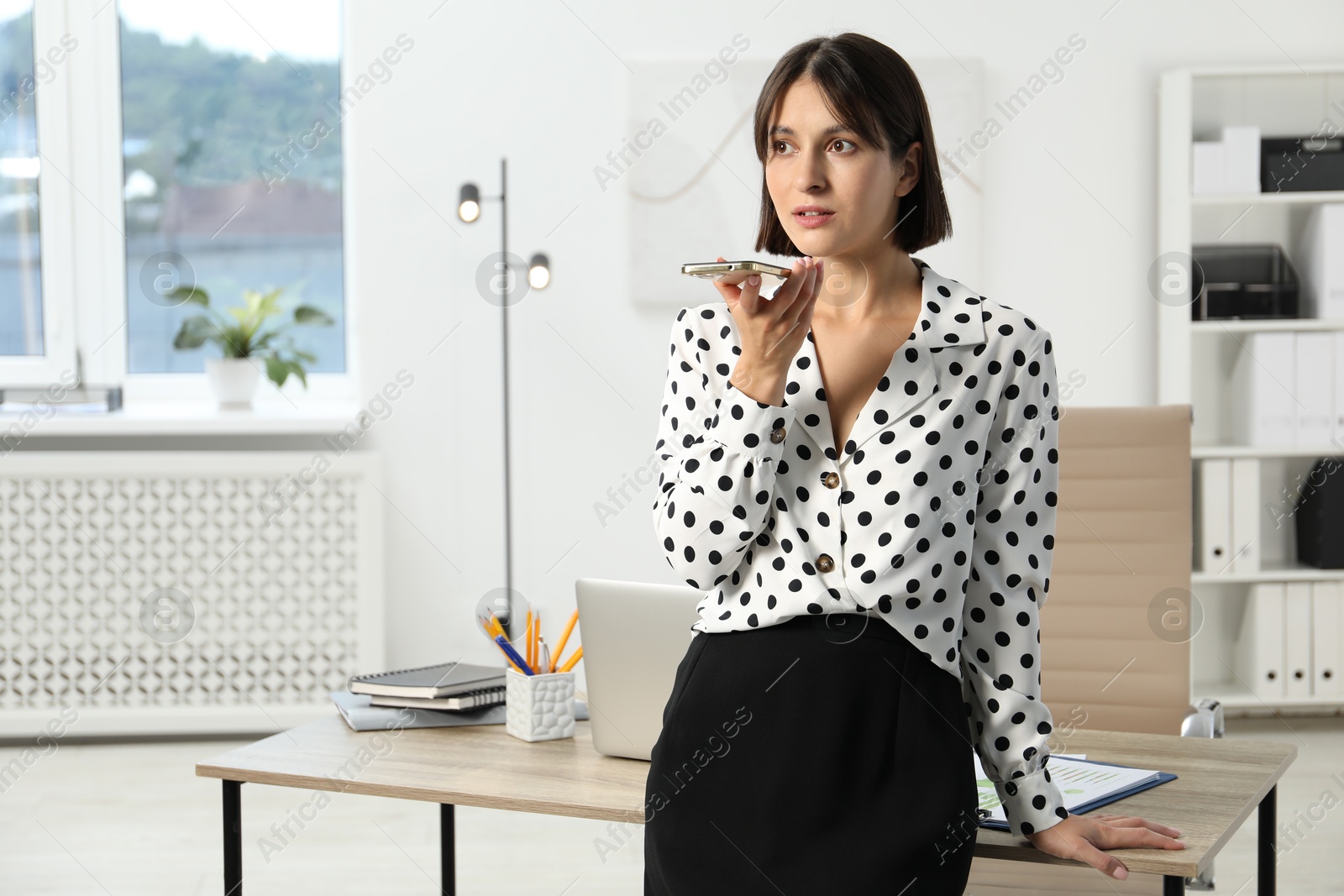 Photo of Beautiful woman recording voice message via smartphone in office