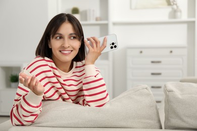 Photo of Beautiful woman with smartphone listening to voice message at home