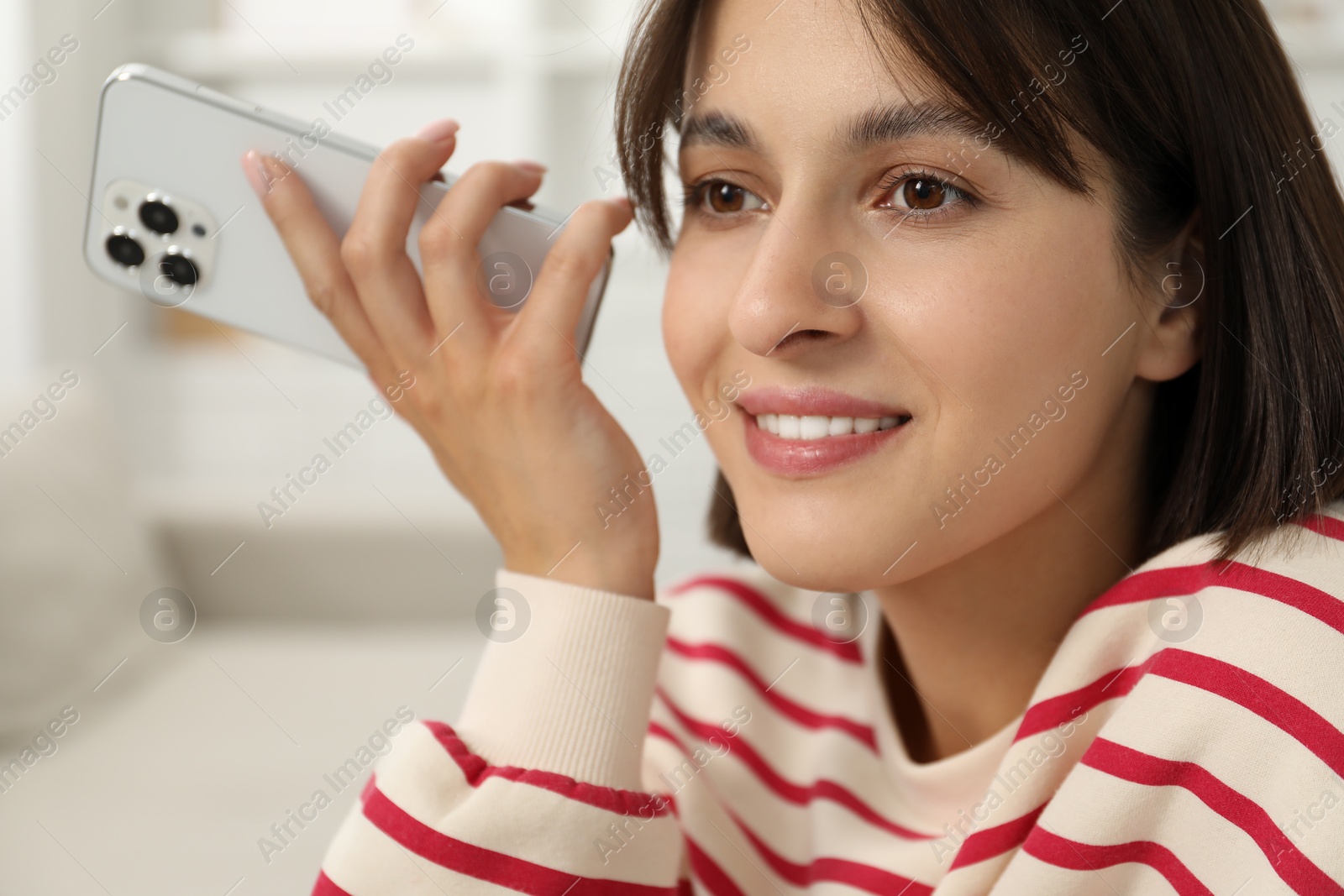 Photo of Beautiful woman with smartphone listening to voice message at home, closeup