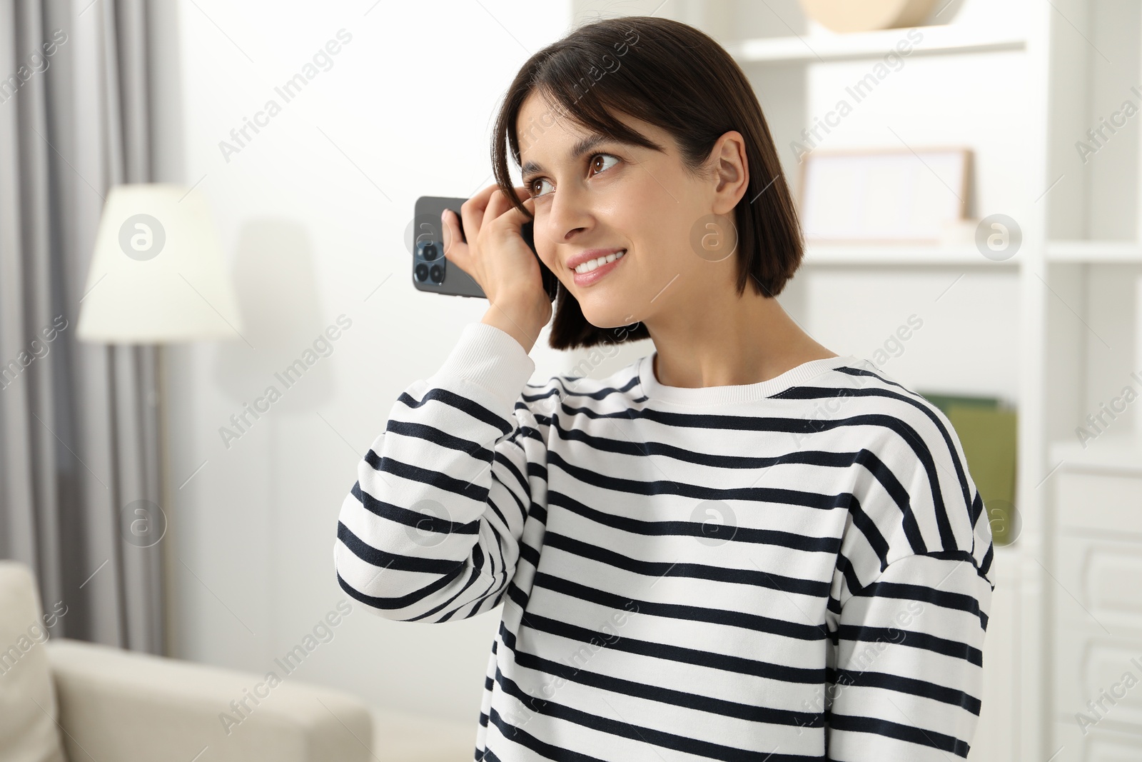 Photo of Beautiful woman with smartphone listening to voice message at home