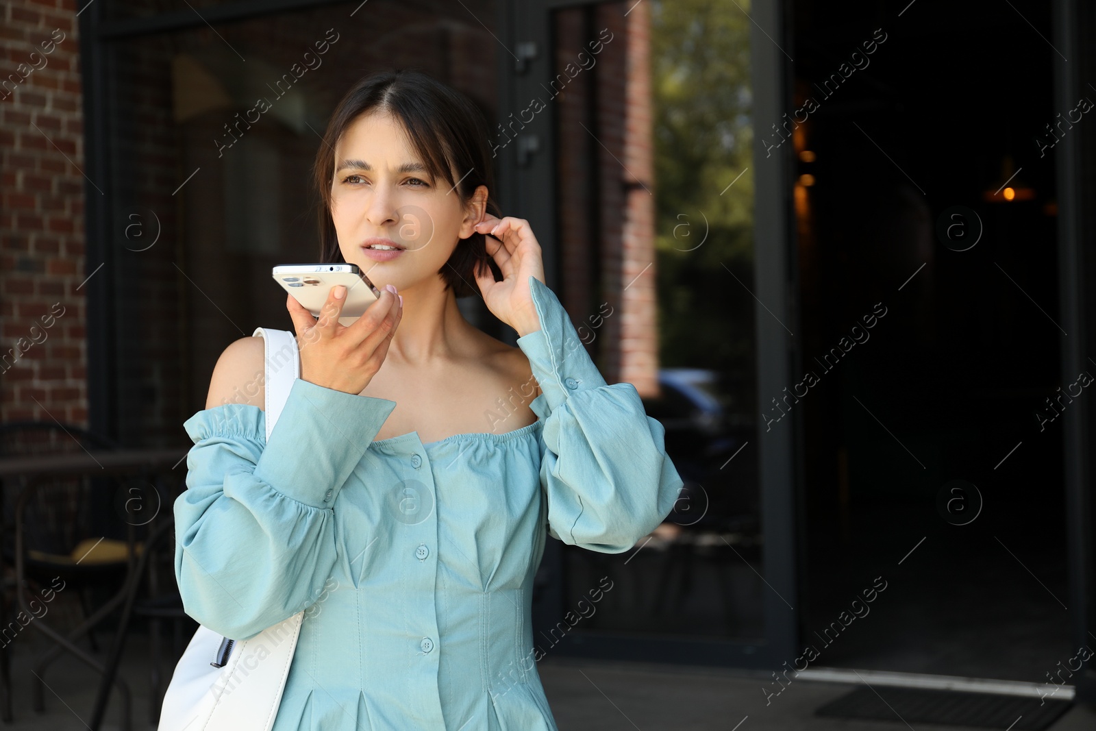 Photo of Beautiful woman recording voice message via smartphone outdoors