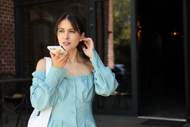 Beautiful woman recording voice message via smartphone outdoors