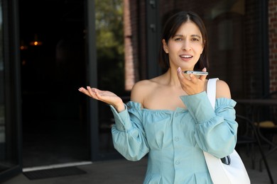 Photo of Beautiful woman recording voice message via smartphone outdoors