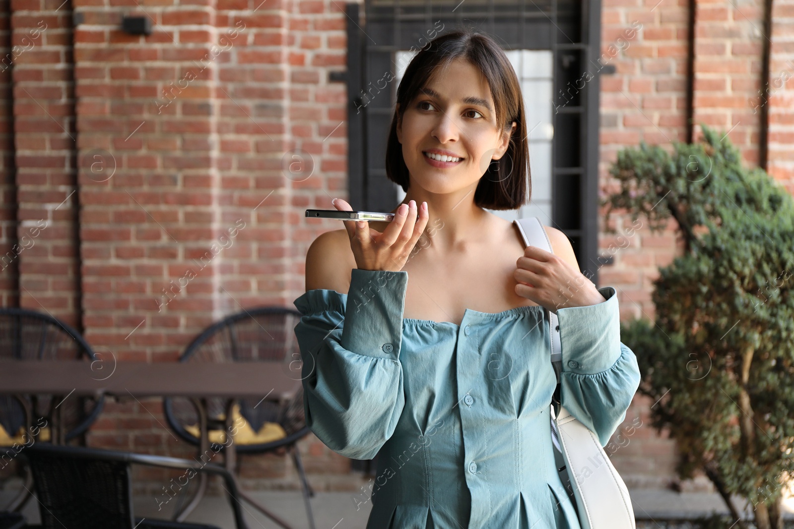 Photo of Beautiful woman recording voice message via smartphone outdoors