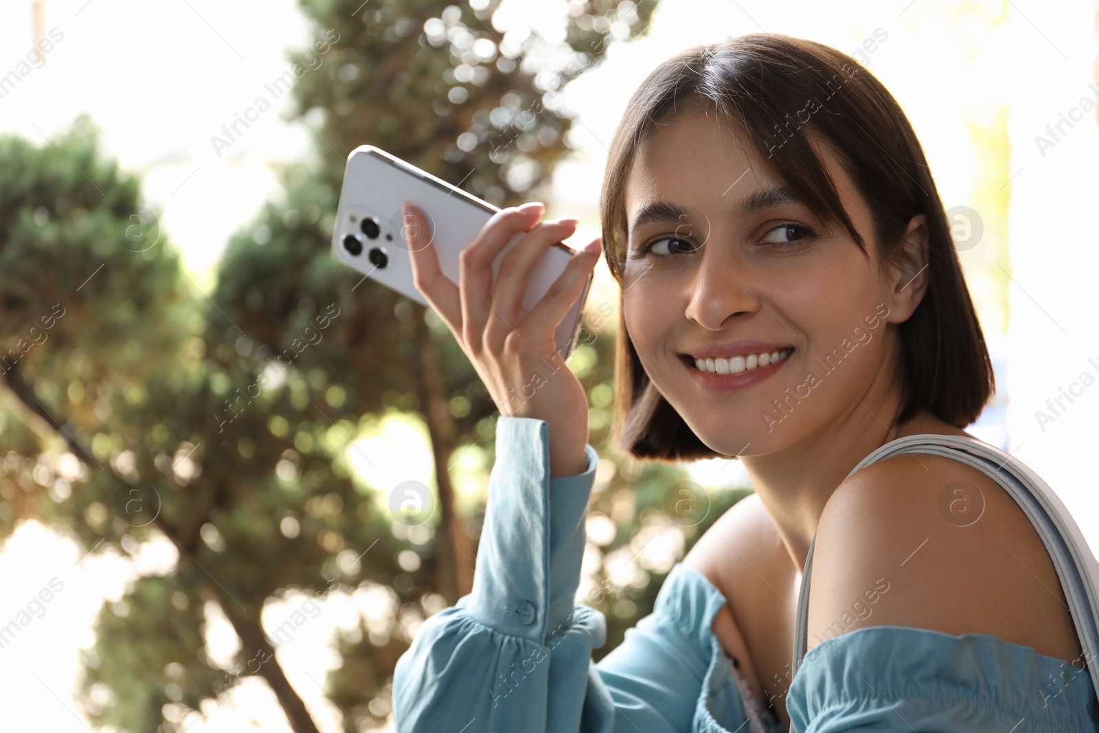 Photo of Beautiful woman with smartphone listening to voice message outdoors