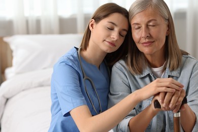 Young healthcare worker supporting senior patient on bed indoors. Space for text