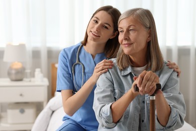 Photo of Smiling healthcare worker supporting senior patient on bed indoors. Space for text