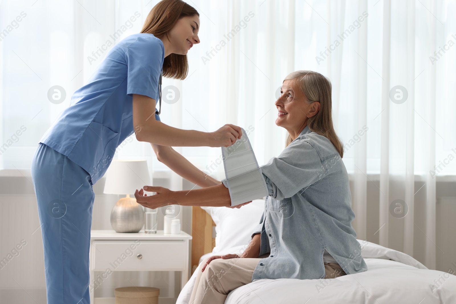 Photo of Smiling healthcare worker measuring patient's blood pressure indoors