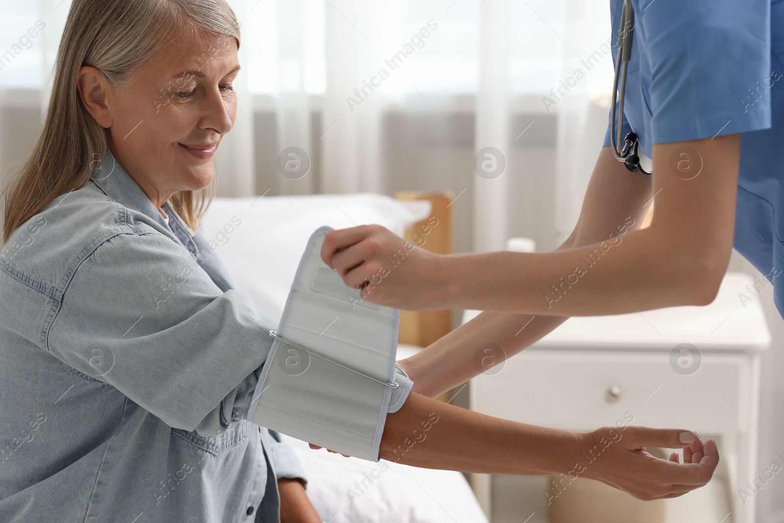 Photo of Healthcare worker measuring patient's blood pressure indoors, closeup