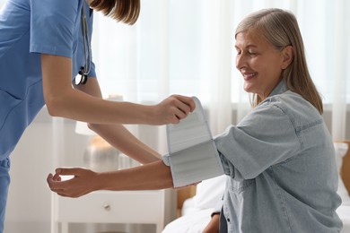 Photo of Healthcare worker measuring patient's blood pressure indoors, closeup