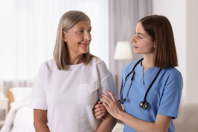 Photo of Young healthcare worker supporting senior patient indoors