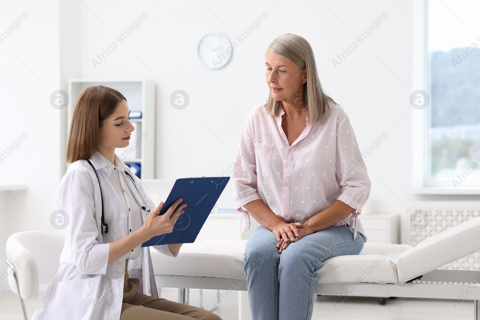 Photo of Young healthcare worker with clipboard consulting senior patient in hospital