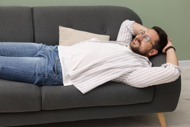 Smiling man with hands behind his head relaxing on sofa at home