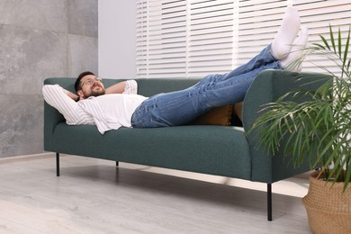 Photo of Smiling man with hands behind his head relaxing on sofa at home