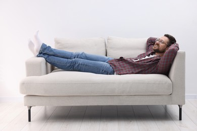 Smiling man with hands behind his head relaxing on sofa at home