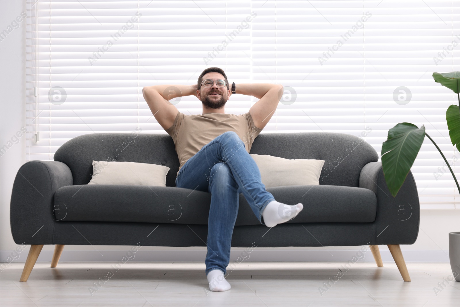 Photo of Smiling man with hands behind his head relaxing on sofa at home