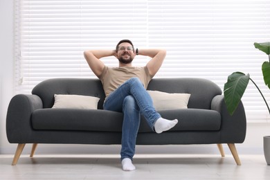 Photo of Smiling man with hands behind his head relaxing on sofa at home