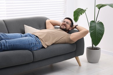 Smiling man with hands behind his head relaxing on sofa at home