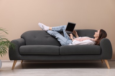 Photo of Smiling woman with laptop lying on sofa at home