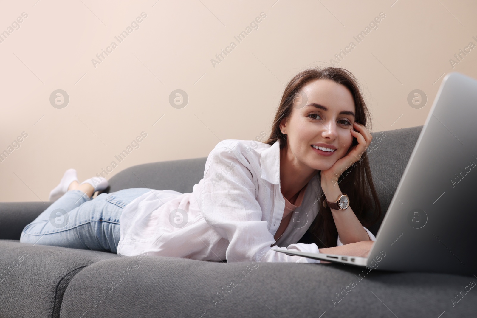 Photo of Smiling woman with laptop lying on sofa at home