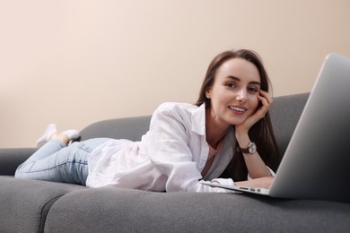 Smiling woman with laptop lying on sofa at home