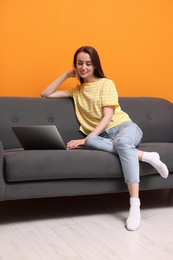 Smiling woman with laptop on sofa at home