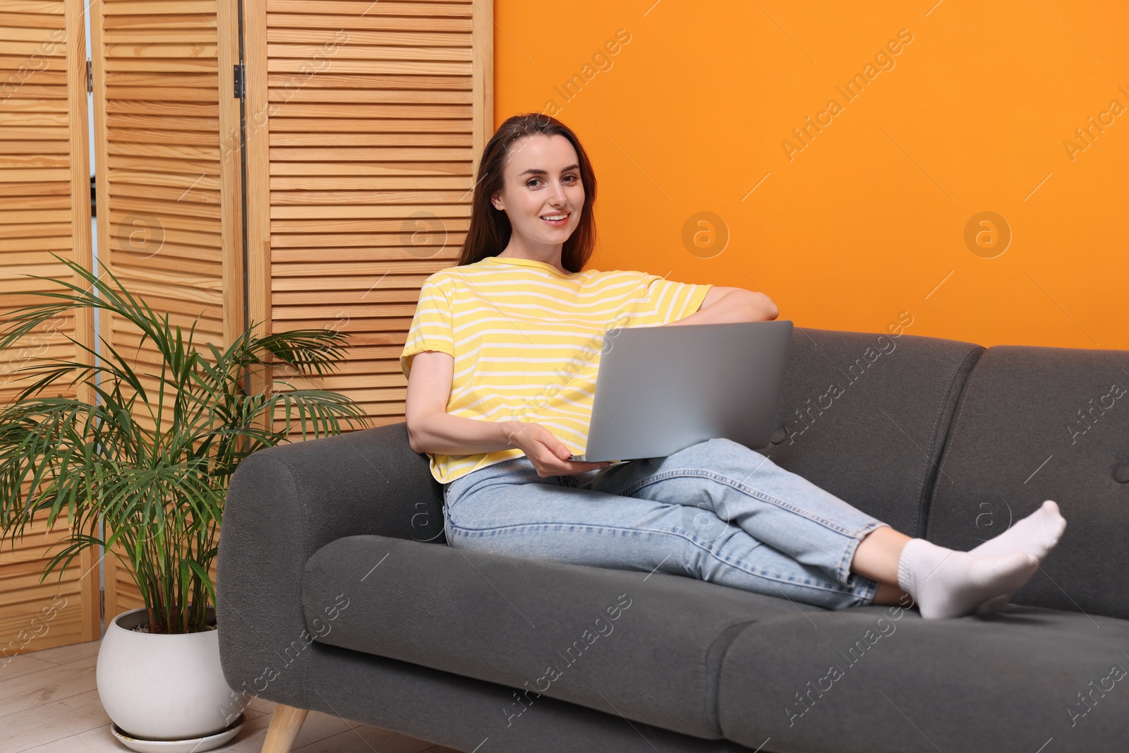 Photo of Smiling woman with laptop on sofa at home