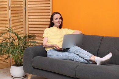 Smiling woman with laptop on sofa at home