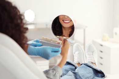 Photo of Patient looking in mirror while doctor holding teeth color chart in clinic, closeup. Dental veneers