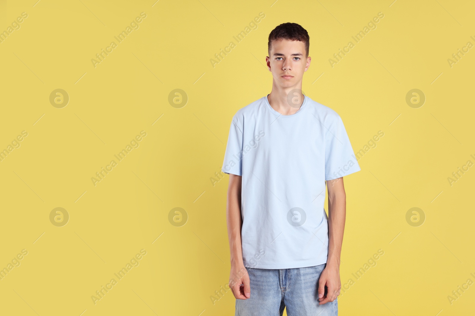 Photo of Teenage boy wearing light blue t-shirt on yellow background, space for text