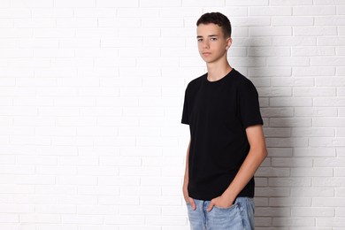 Teenage boy wearing black t-shirt near white brick wall, space for text