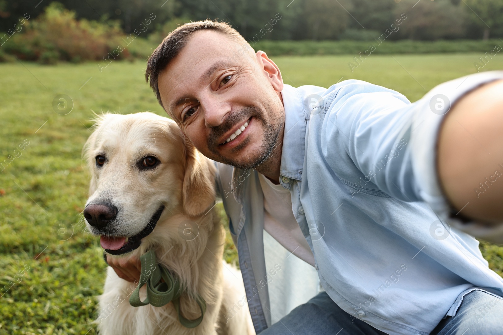 Photo of Smiling man with cute Golden Retriever dog taking selfie on spring day