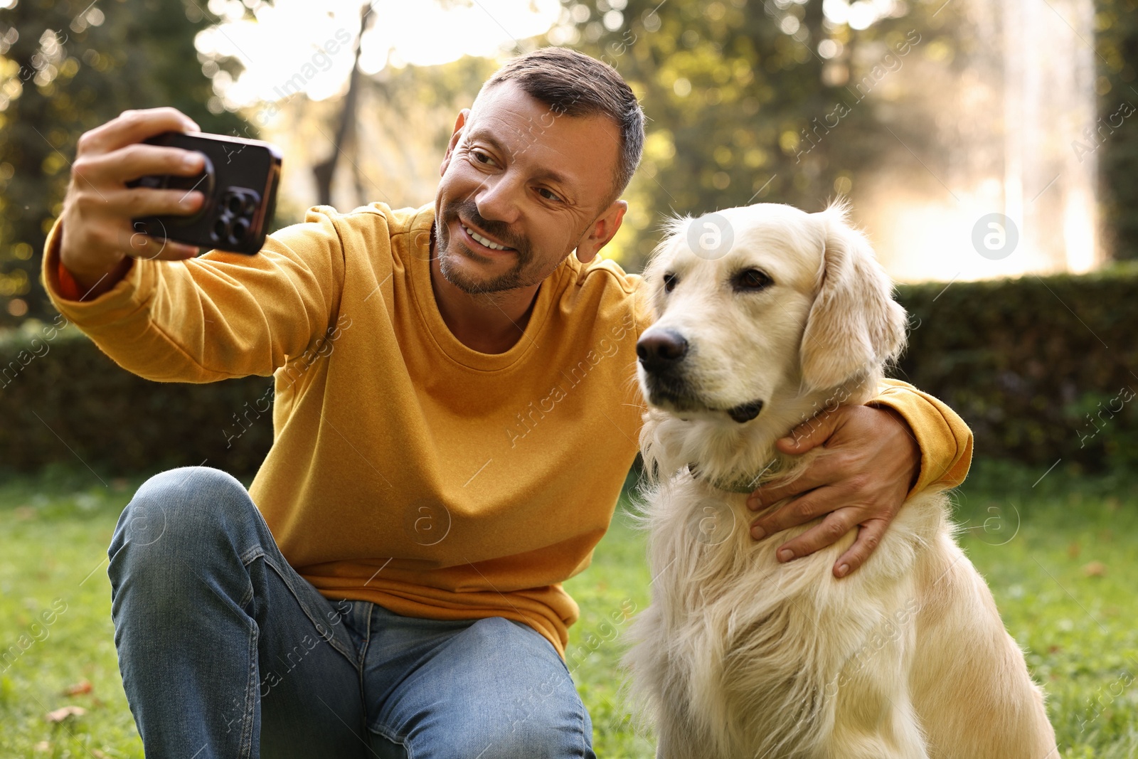 Photo of Smiling man with cute Golden Retriever dog taking selfie on spring day