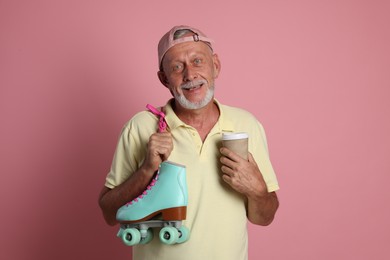 Photo of Portrait of happy senior man with paper cup and roller skates on pink background